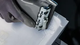 Person wearing safety equipment uses a power tool to smooth the edge of a white material.