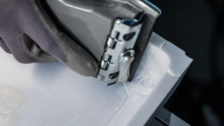 Person wearing safety equipment uses a power tool to smooth the edge of a white material.