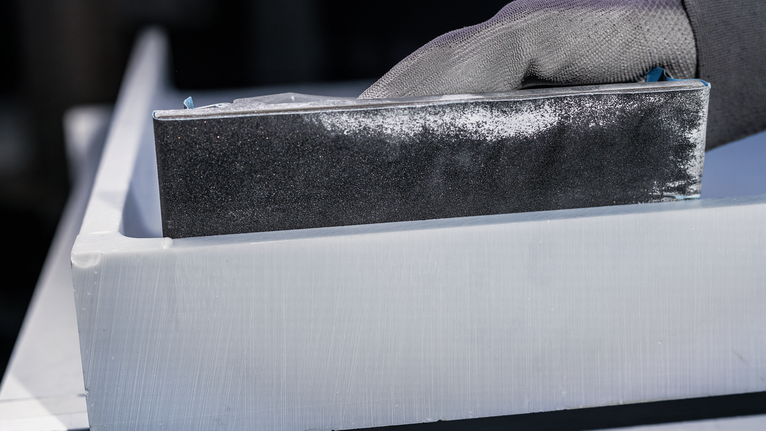 Person wearing safety equipment sands a white plastic edge with a sanding block.