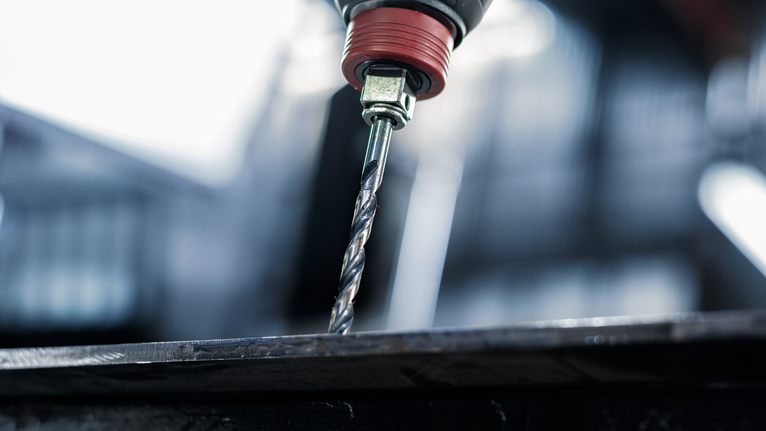 A power drill making a hole in a metal sheet.