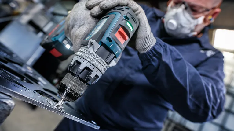 Person wearing safety equipment drilling into metal sheet.