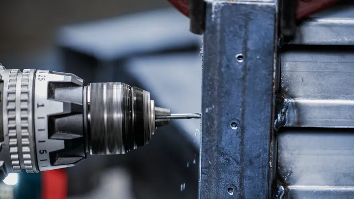 Drill making holes in a metal beam.