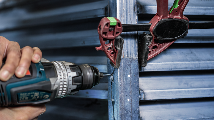 Person using a power drill to fasten metal panels secured by clamps.