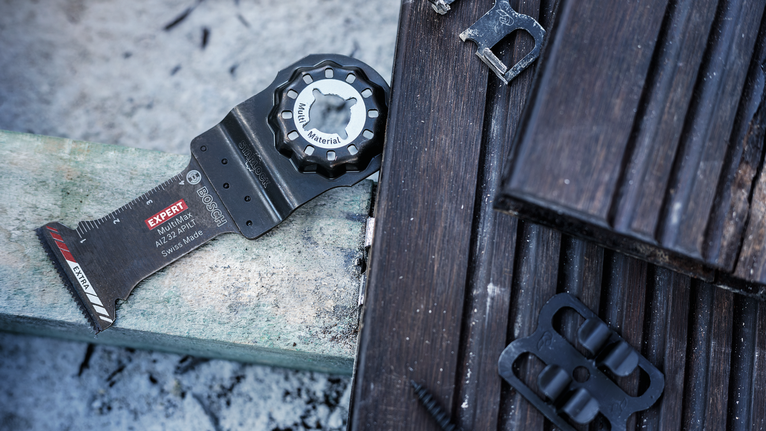 Oscillating multi-tool blade placed on wood planks outdoors.