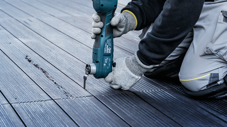 Person wearing safety equipment uses a power tool to cut grooves in wooden decking.