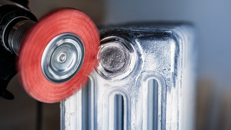 Red abrasive wheel grinding a metal radiator surface.