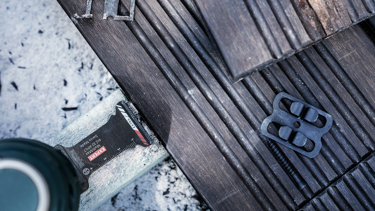 Oscillating tool cutting a wooden deck board near a fastener.