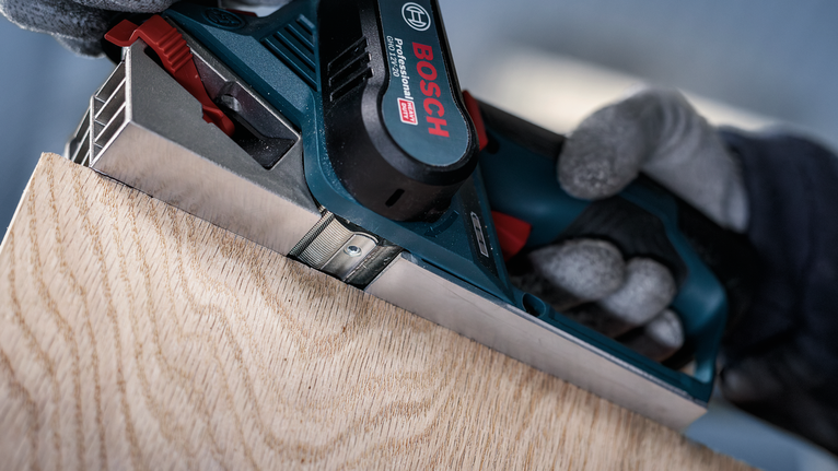 Person wearing safety equipment planes the edge of a wooden board.