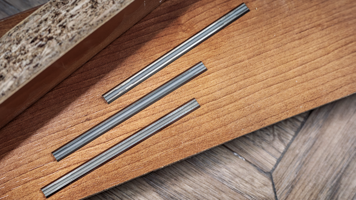 Three parallel grooves cut into a wooden board on a parquet floor.