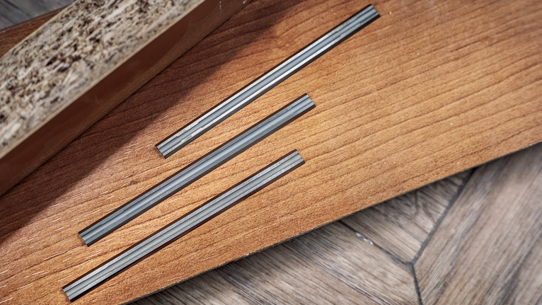 Three parallel grooves cut into a wooden board on a parquet floor.