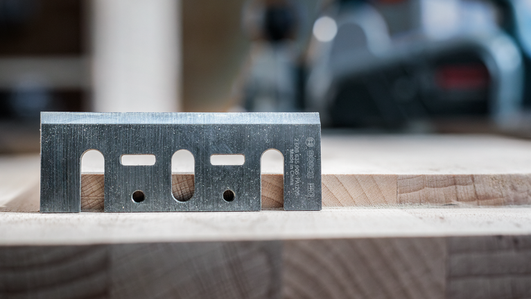 Metal planer blade resting on a piece of wood in a workshop.