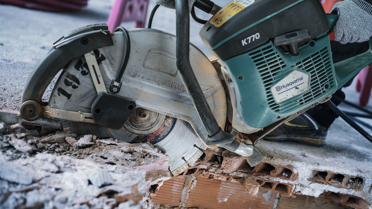A person wearing safety equipment cuts through concrete blocks with a circular saw.