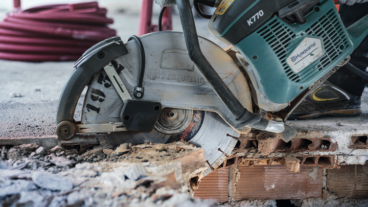 A person wearing safety equipment cuts through brick with a diamond saw blade.