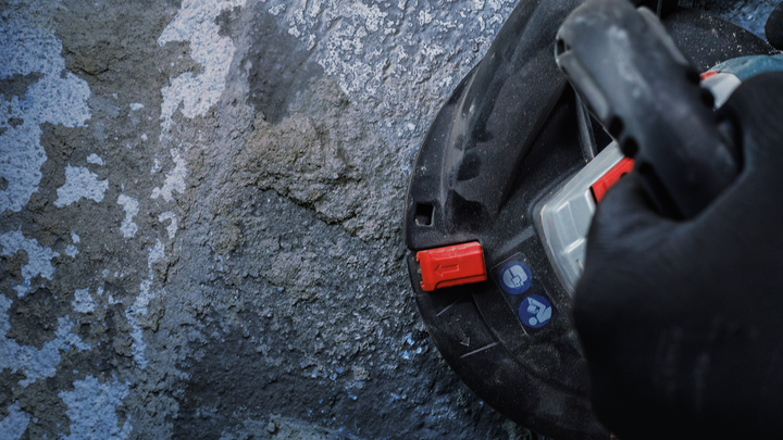 Person wearing safety equipment operates a tool against a rough concrete surface.