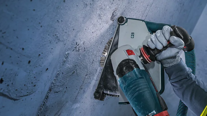 Person wearing safety equipment cuts a groove into concrete with a power tool.
