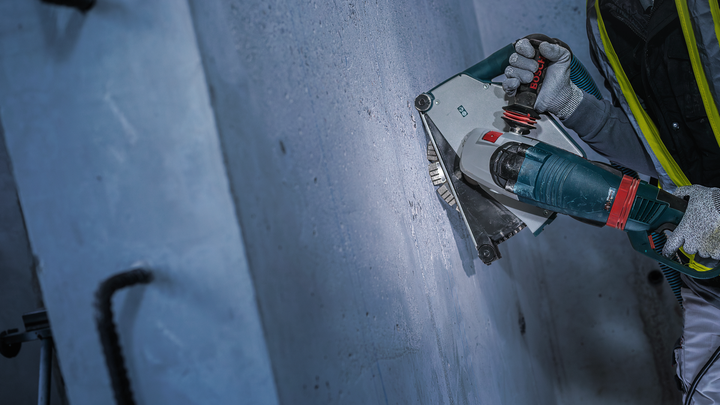 A person wearing safety equipment cuts a groove into a concrete wall with a power tool.