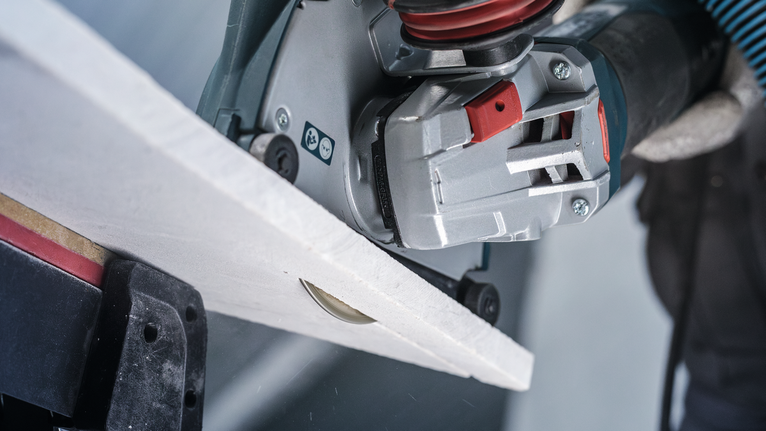Person wearing safety equipment cuts a tile with a handheld power cutter.