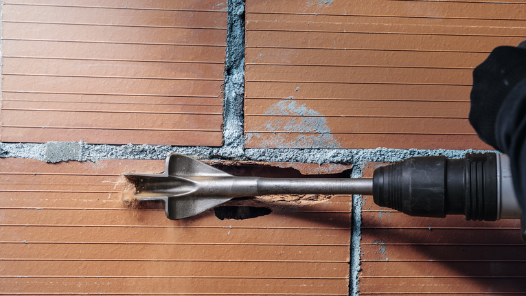 Person wearing safety equipment chisels a groove into a tiled brick wall.
