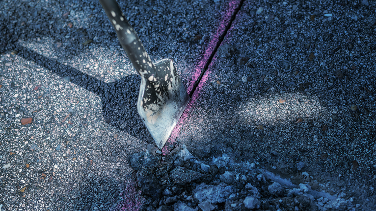 Chisel breaking concrete along a marked line.