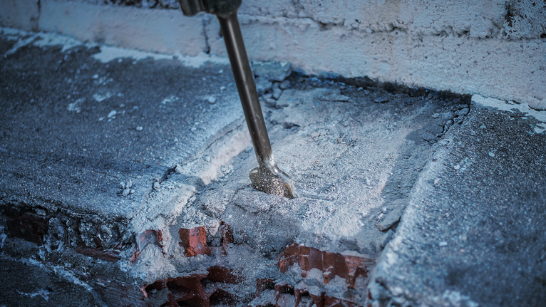 Demolition hammer breaking through a concrete and brick wall.