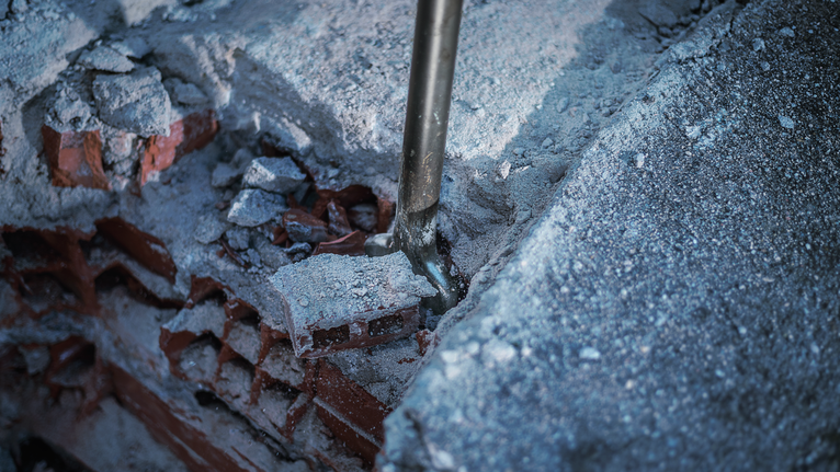 Chisel breaking through concrete and brick debris.