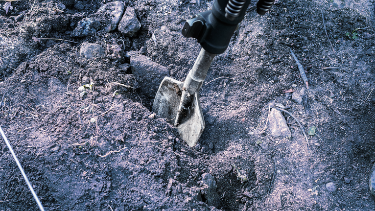 A demolition tool breaks up soil and rocks on the ground.