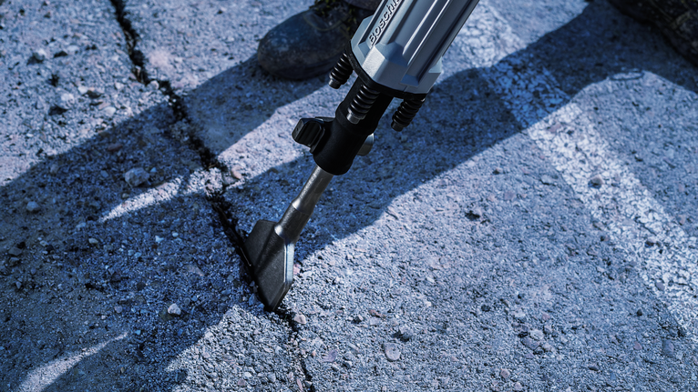 Demolition hammer breaking a crack in concrete pavement.