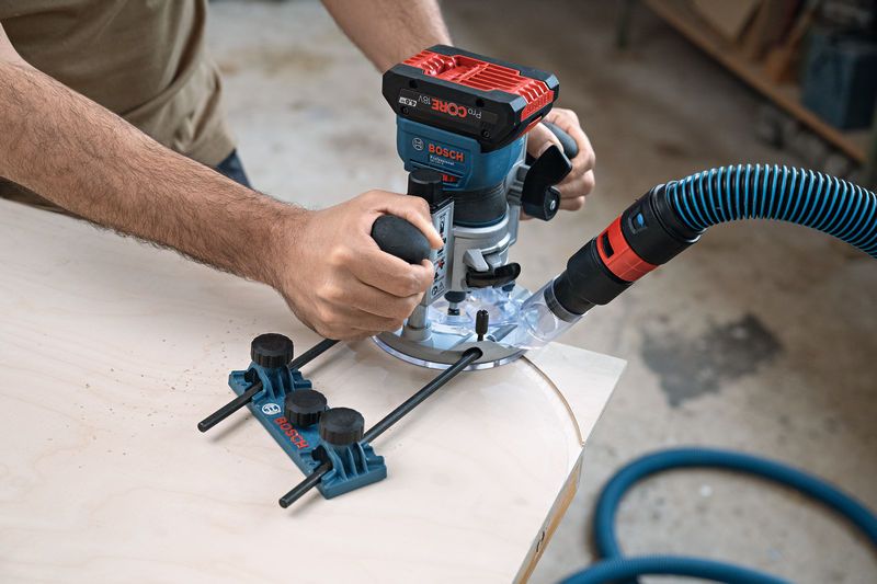 A person guides a cordless palm router along a curved wooden edge in a workshop.