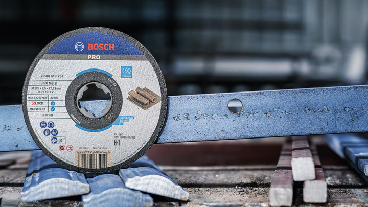 Cutting disc placed upright next to a metal bar with a hole in a workshop.