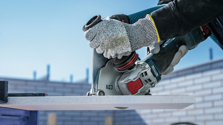 Person wearing safety equipment uses a power tool to cut a white board.