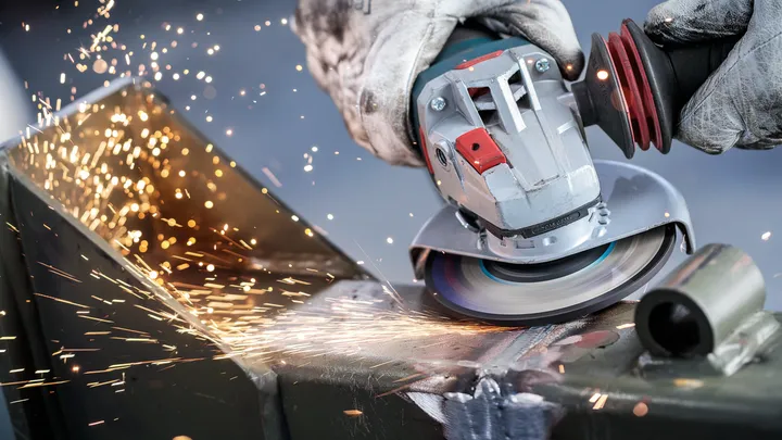Person wearing safety equipment grinds metal, producing bright sparks.