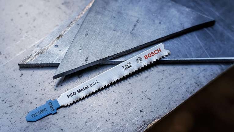 Metal saw blade resting on a steel surface next to cut metal sheets.