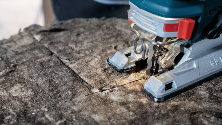 A jigsaw making a straight cut through a rough wooden surface.