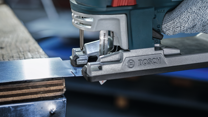 Person wearing safety equipment cuts metal sheet with a jigsaw.