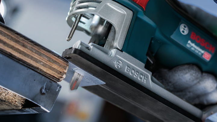 A person wearing safety equipment uses a power jigsaw to cut wood.