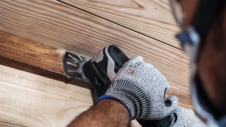 Person wearing safety equipment sands wooden boards with a power tool.