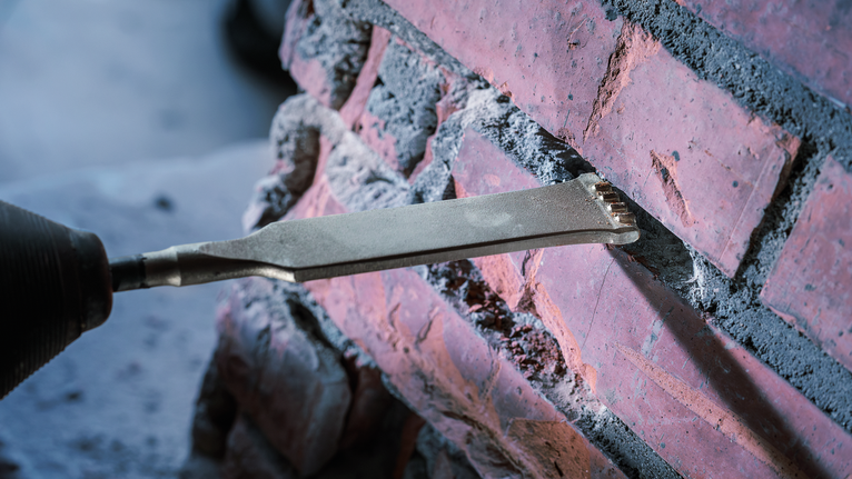Chisel removing mortar from brick wall.