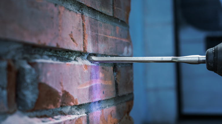 Chisel attachment removing mortar from between bricks on a wall.