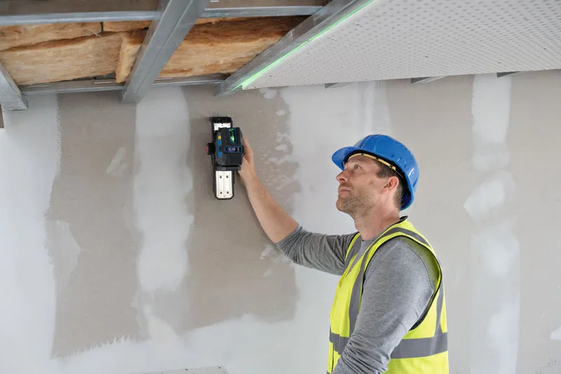 Person wearing safety equipment uses laser leveling tool to align drywall ceiling.