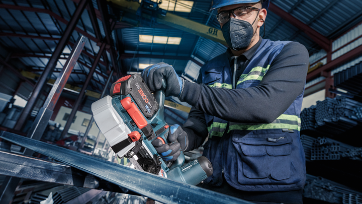 A person wearing safety equipment cuts metal with a cordless power saw.