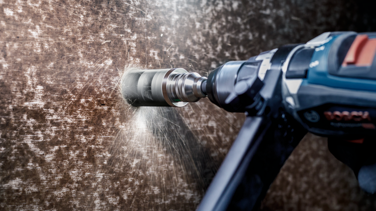 Rotary hammer drills into a metal surface, creating sparks.
