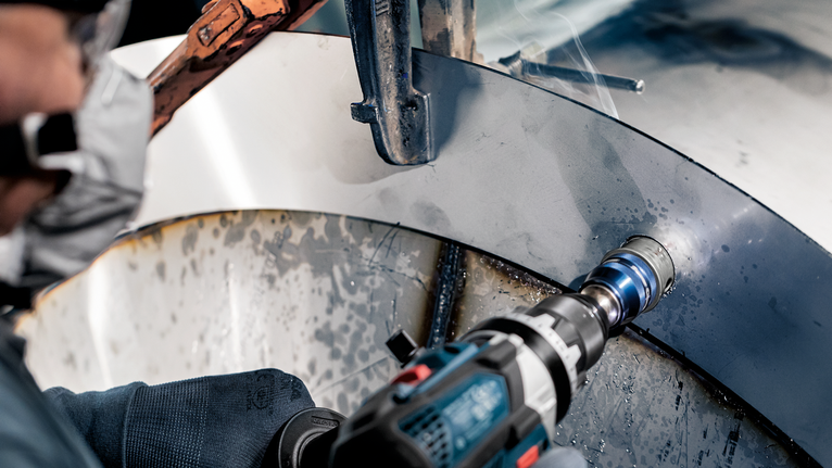 Person wearing safety equipment drills a hole into a curved metal surface.