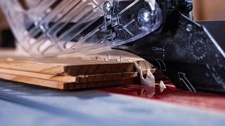 Circular saw blade cutting through stacked wood boards in a workshop.