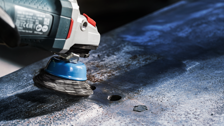 Wire cup brush tool grinding rust off a metal surface.