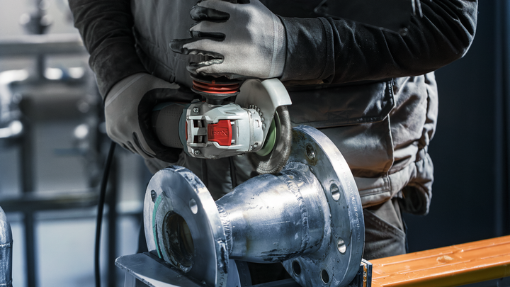 Person wearing safety equipment grinds a metal pipe with an angle grinder.