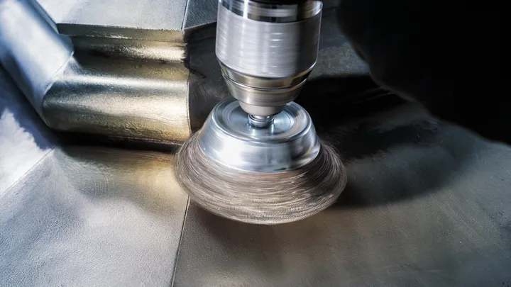 A person polishes a metal surface using a rotary brush attachment.