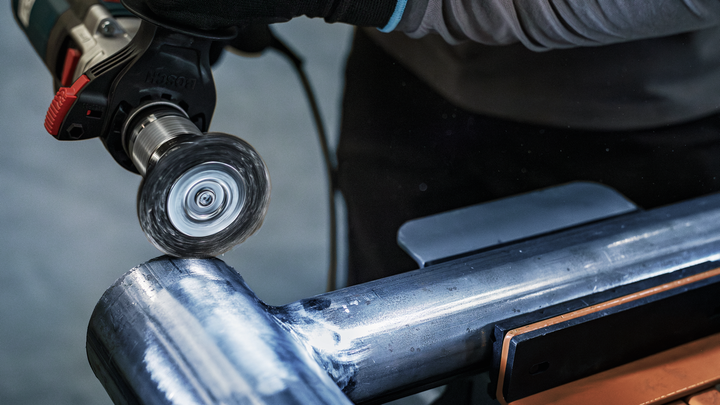 Person wearing safety equipment polishes a large metal pipe with a power tool.