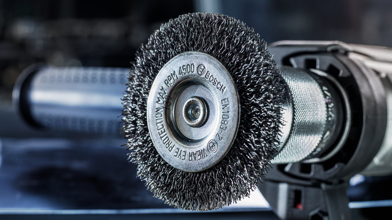Wire brush attachment on a power tool for surface cleaning or rust removal.