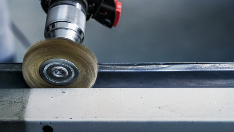 Wire brush attachment polishing the edge of a steel beam.