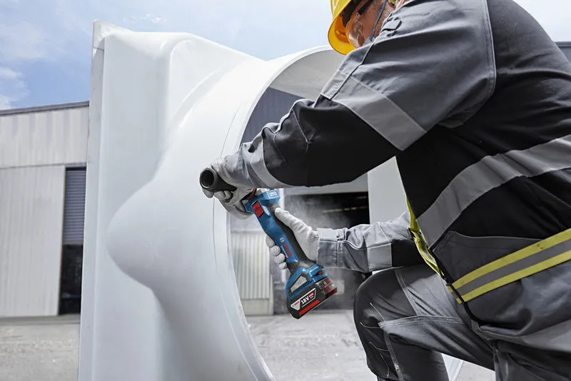 A person wearing safety equipment grinds the edge of a large metal tube outdoors.